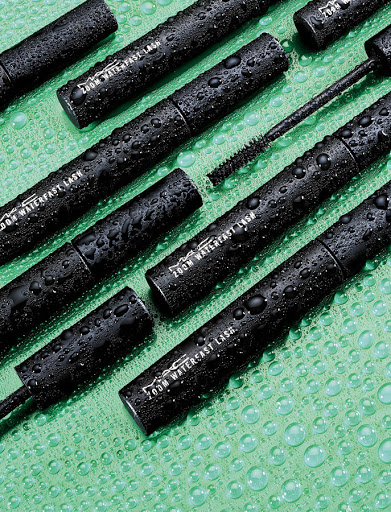 MAC Zoom Waterfast Lash mascara tubes and applicators on a patterned green background, product shot, beauty and cosmetics advertising.