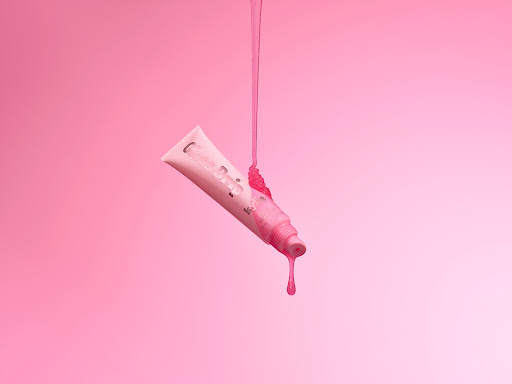 Pink lip gloss tube with dripping gloss against a gradient pink background, beauty product, cosmetic advertisement, minimal.