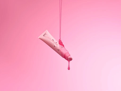 Pink lip gloss tube with dripping gloss against a gradient pink background, beauty product, cosmetic advertisement, minimal.