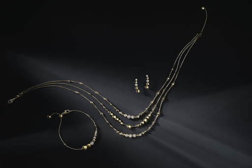 Elegant gold necklace, bracelet, and earrings jewellery set on a shiny black surface with soft lighting, a stylish accessory.