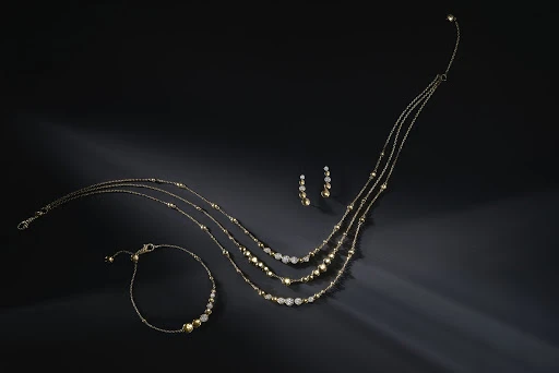 Elegant gold necklace, bracelet, and earrings jewellery set on a shiny black surface with soft lighting, a stylish accessory.