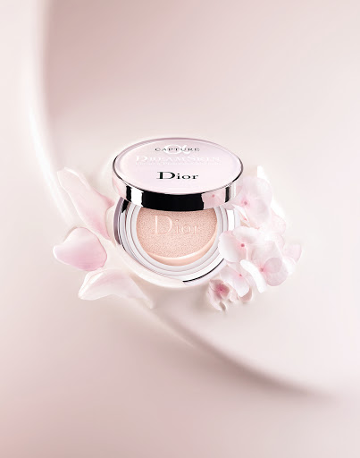 Dior Capture Dreamskin cushion foundation compact with pale pink floral accents on a smooth, gradient pink background.