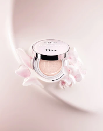 Dior Capture Dreamskin cushion foundation compact with pale pink floral accents on a smooth, gradient pink background.