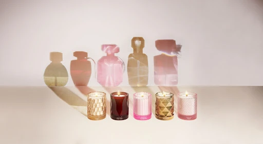 Five decorative candles displayed against a soft background, with shadow outlines of perfume bottles enhancing the product presentation.