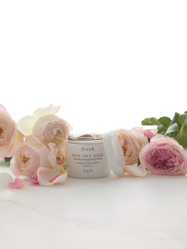 Fresh Rose Face Mask container with lid near pink roses and petals on a white surface, product shot for beauty or skincare brand.
