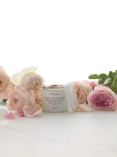 Fresh Rose Face Mask container with lid near pink roses and petals on a white surface, product shot for beauty or skincare brand.