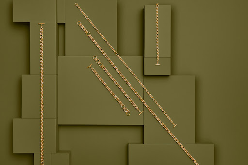Arrangement of gold necklaces on a background of olive green rectangular blocks. Jewellery, accessories, luxury, and simple.