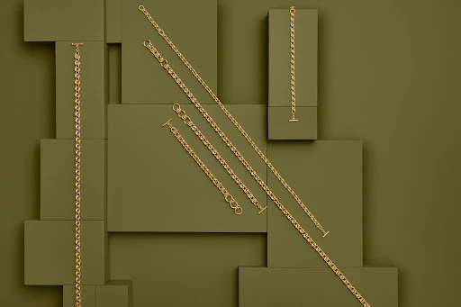 Arrangement of gold necklaces on a background of olive green rectangular blocks. Jewellery, accessories, luxury, and simple.