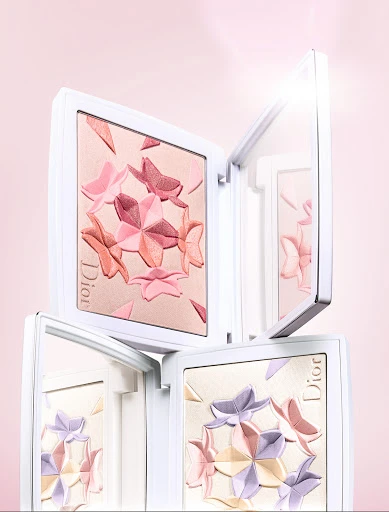 Stacked Dior makeup compacts with butterfly designs in a pastel color palette against a light pink background. Beauty and cosmetics.