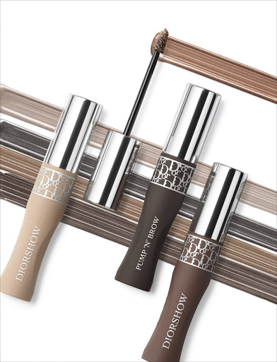 Three tubes of Dior Diorshow Pump 'N' Brow brow mascara are displayed on a white surface with swipes of brown mascara.