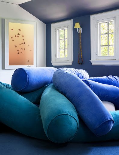 Interior with blue and teal cylindrical cushions on a blue surface, lit by natural window light, with blue walls and ceiling.