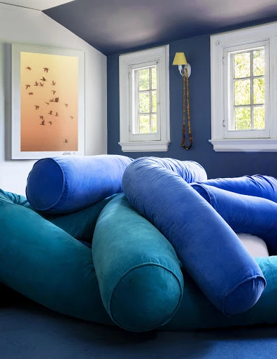 Interior with blue and teal cylindrical cushions on a blue surface, lit by natural window light, with blue walls and ceiling.