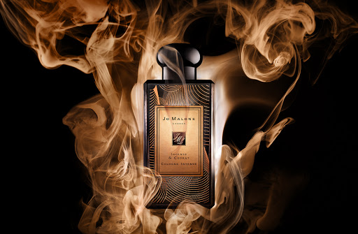 Elegant perfume bottle by Jo Malone London, featuring a sleek design and amber liquid against a dramatic backdrop of swirling smoke.
