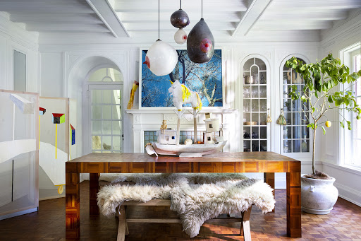 Interior of a dining room with a wood table, bench, and artwork, featuring a decorative lemon tree and modern light fixtures.