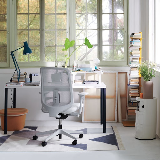 Office chair in a well-lit room with a desk, books, and large windows, offering a view of trees and natural light.