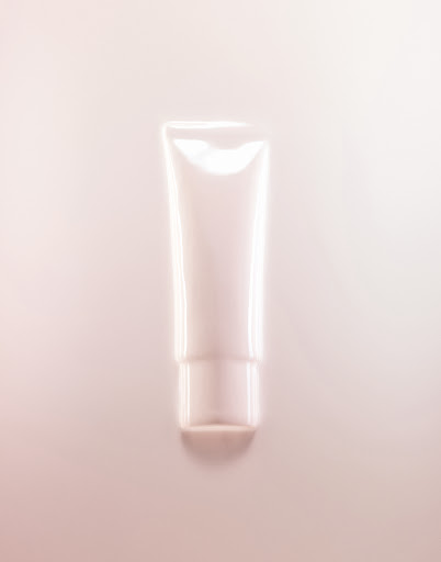 A cosmetic tube of cream or lotion is displayed against a light pink background, suitable for beauty, skincare, or product advertising.