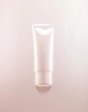 A cosmetic tube of cream or lotion is displayed against a light pink background, suitable for beauty, skincare, or product advertising.
