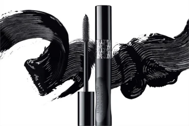 Black mascara tube and wand standing vertically against a bright white background with dramatic black mascara brush strokes