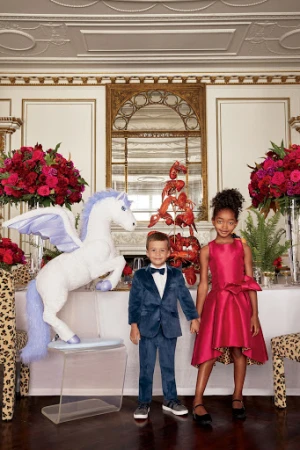 Young boy in blue velvet suit and girl in pink dress standing before a winged white pegasus prop and floral arrangements