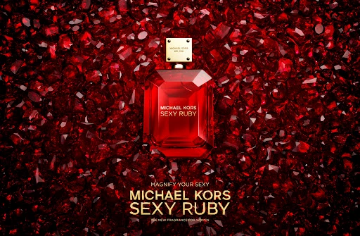 Red perfume bottle of Michael Kors Sexy Ruby resting on a sea of glistening deep red gemstones