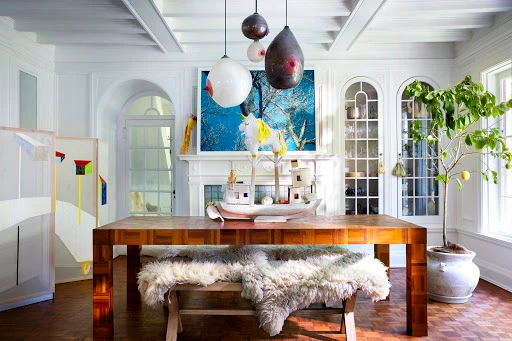 Interior dining room featuring a wooden table with fur benches, unique pendant lights, and a framed blue landscape artwork.