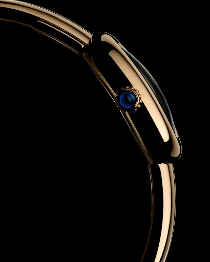 Close-up of a gold watch with a distinctive blue jewel accent, set against a stark black background, highlighting its sleek design.