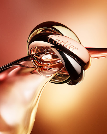 Close-up studio shot of three entwined gold Cartier rings with the brand name visible. The rings rest on a blurred gold background.