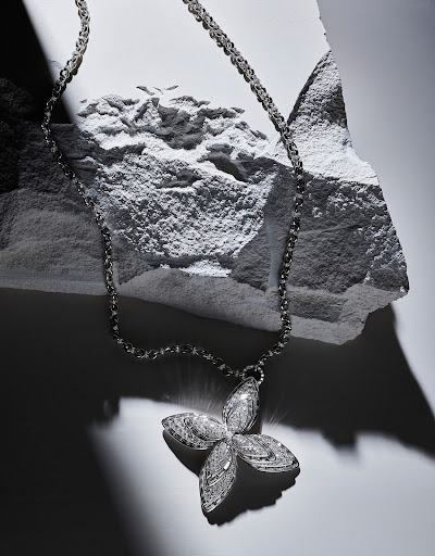 Elegant silver necklace with a four-leaf clover pendant displayed on a textured white stone surface under soft lighting.