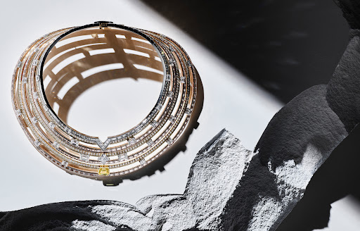 High fashion gold choker necklace with sparkling gemstones on a studio set, accented with black and grey rocky material.