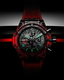 Close-up product shot of a luxury transparent red wristwatch with a skeleton dial against a dark background.