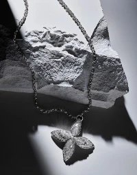 Sparkling diamond flower pendant necklace draped over rugged grey stone texture with dramatic light and shadow.