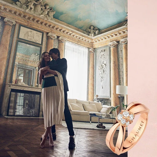 Jewelry advertisement featuring a man and woman embracing inside an ornately decorated room, with a close-up of a ring. 