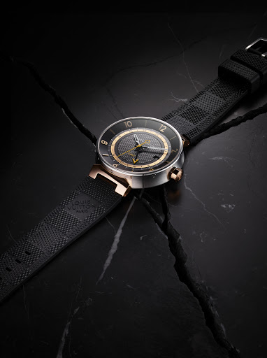 Luxury black wristwatch with gold accents displayed on dark marble with a textured rubber strap and a square patterned design on the band.