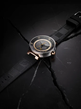 Luxury black wristwatch with gold accents displayed on dark marble with a textured rubber strap and a square patterned design on the band.