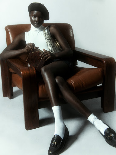 Woman in beret poses in leather armchair in a fashion shot with vintage flair, displaying retro fashion elements in a studio setting.