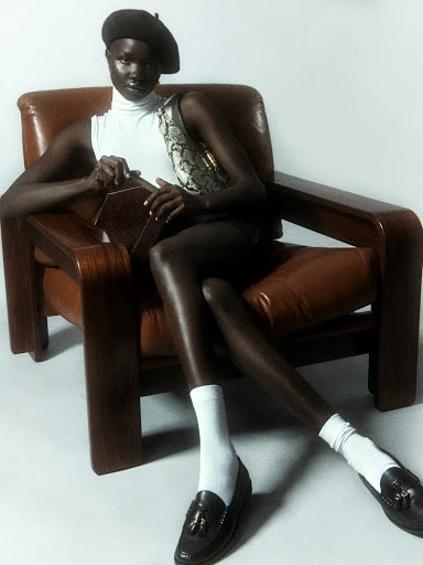 Woman in beret poses in leather armchair in a fashion shot with vintage flair, displaying retro fashion elements in a studio setting.