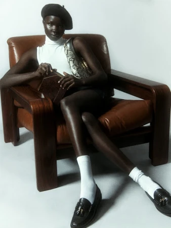 Woman in beret poses in leather armchair in a fashion shot with vintage flair, displaying retro fashion elements in a studio setting.