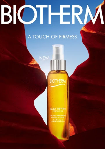 Biotherm Body Refirm Stretch Oil bottle in skincare product shot against blurred rock formations and a bright blue sky background.