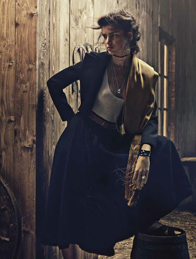 Model in dark jacket, white top, and long skirt leaning against a wooden barn wall styled by Sylvain Cabouat