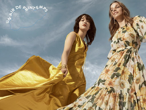 Two models wearing vibrant yellow dresses outdoors against a bright blue sky with soft white clouds