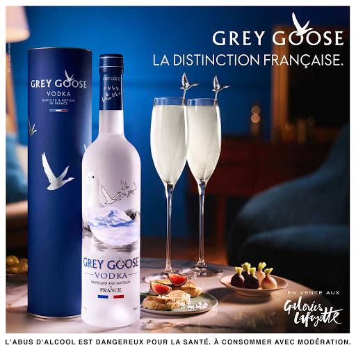Grey Goose Vodka bottle and presentation with flute glasses and snacks on a marble surface in an indoor setting with blue lighting.