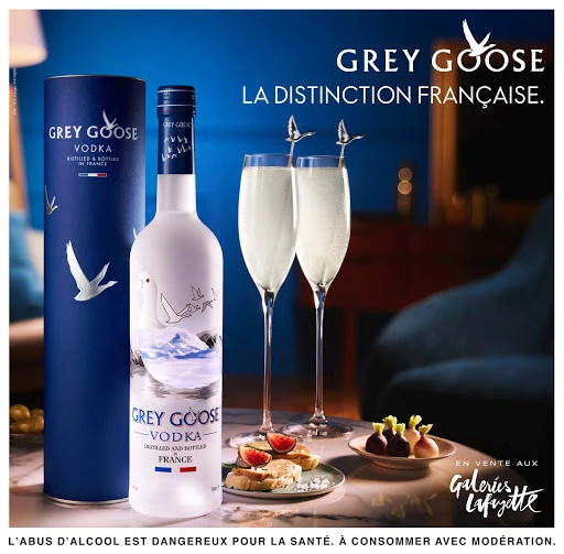 Grey Goose Vodka bottle and presentation with flute glasses and snacks on a marble surface in an indoor setting with blue lighting.