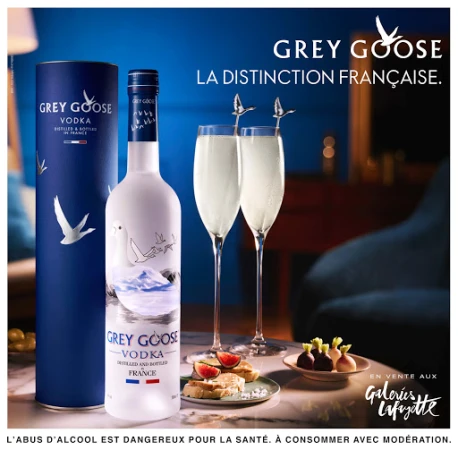 Grey Goose Vodka bottle and presentation with flute glasses and snacks on a marble surface in an indoor setting with blue lighting.