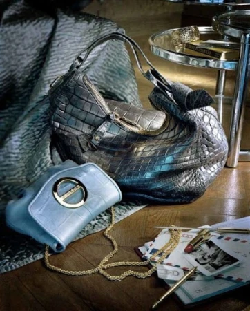 Still life with textured leather handbags, silver side table, stationery, and lipstick on a wood floor in a warm, inviting indoor setting.