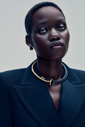 Striking portrait of a woman with short dark hair wearing a sophisticated black blazer and a unique gold and black necklace.
