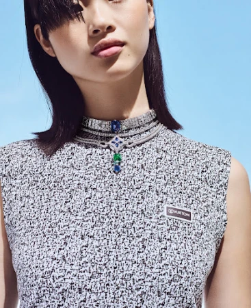 Close-up portrait of a woman wearing layered diamond necklaces and a patterned top against a clear blue sky background.