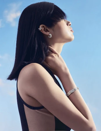 Profile portrait of a woman with heavy blunt bangs wearing diamond jewelry against a clear sky