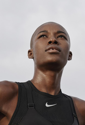 Close-up of a Black woman wearing a black Nike athletic top with a white logo, looking upwards towards a bright sky.