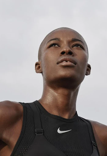 Close-up of a Black woman wearing a black Nike athletic top with a white logo, looking upwards towards a bright sky.