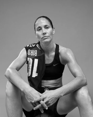 Portrait of Sue Bird wearing a sports bra and towel over her shoulder, posed against a solid grey background